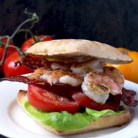 A sandwich with grilled shrimp in herb aioli with tomatoes, bacon and lettuce