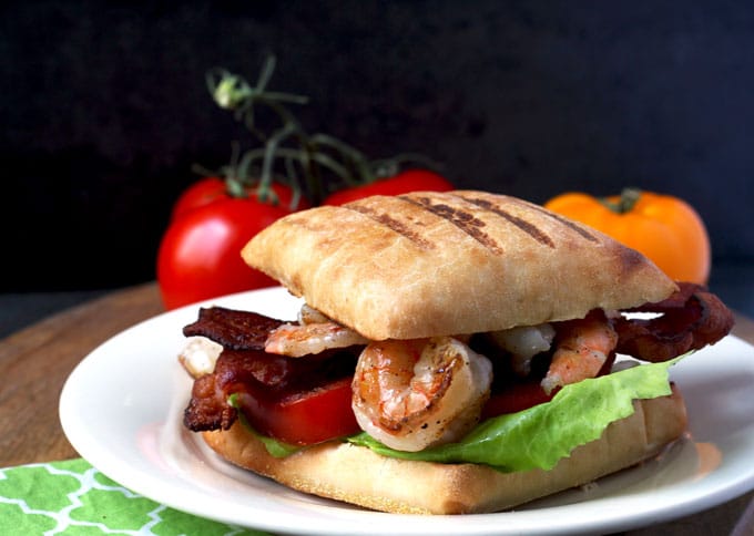 A panini sandwich with grilled shrimp in herb aioli with tomatoes, bacon and lettuce 