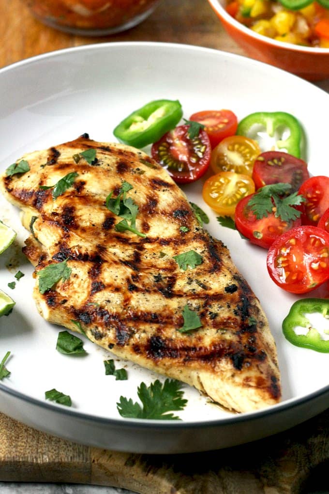 Grilled chicken breast half served with tomatoes on a white plate.