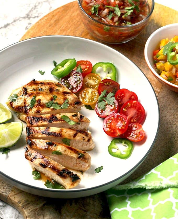 Sliced grilled tequila chicken served with fresh tomatoes on a white plate.