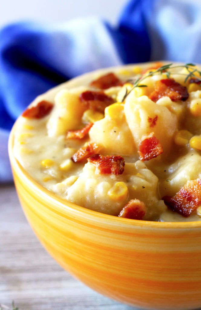 Close up view of the potato corn chowder on an orange ceramic bowl topped with crispy bacon pieces