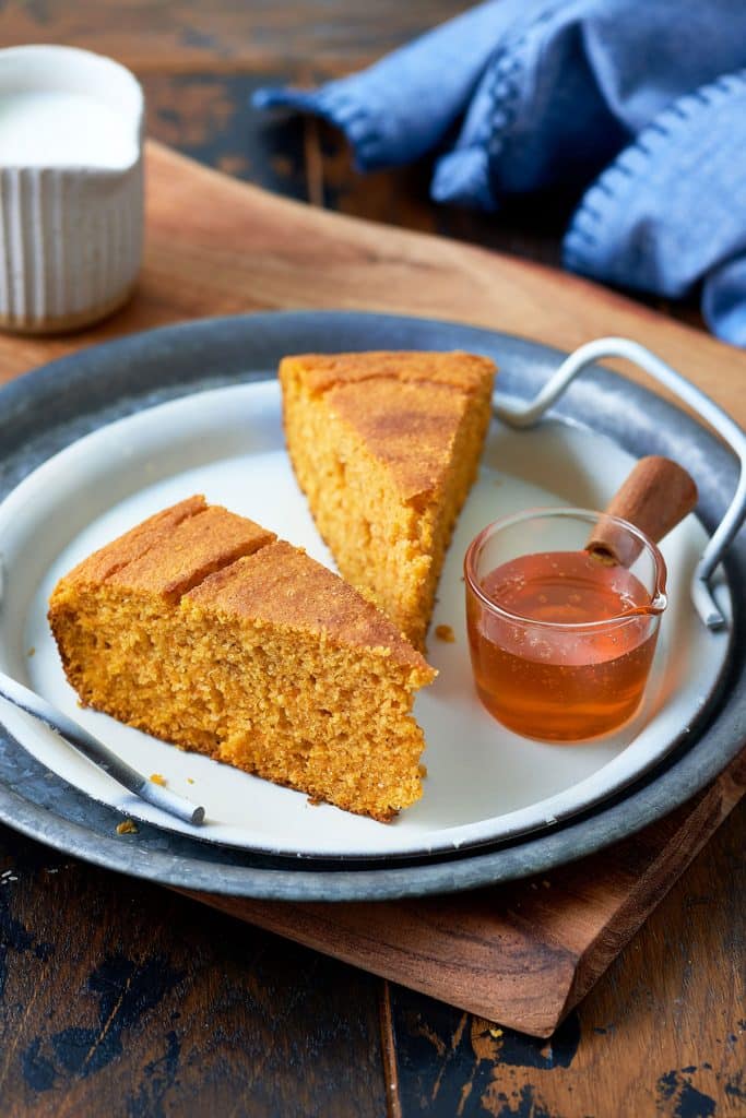 Two slices of Cornbread on a plate next to a small pot with honey