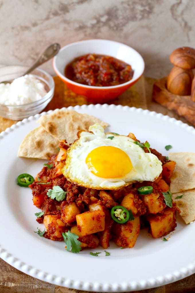 Potato and Chorizo Hash served on a white plate with a fried sunny side up egg and tortillas