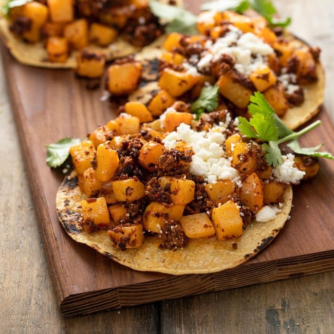 Papas and chorizo tacos on corn tortillas set on a wooden board.