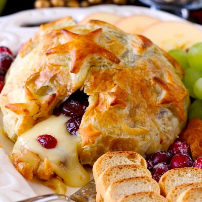 Melted Baked Brie with Cranberries served with fruits and crackers on a white plate.