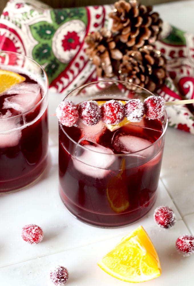 Close up view of an old fashioned type glass filled with Cranberry Maple Bourbon Cocktail. Sugared cranberries are skewered on a small cocktail pick. 