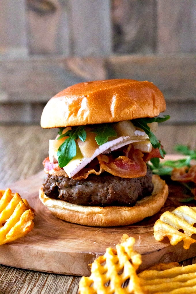 View of a burger with pancetta, brie cheese, sliced pears and arugula in a wooden plate.