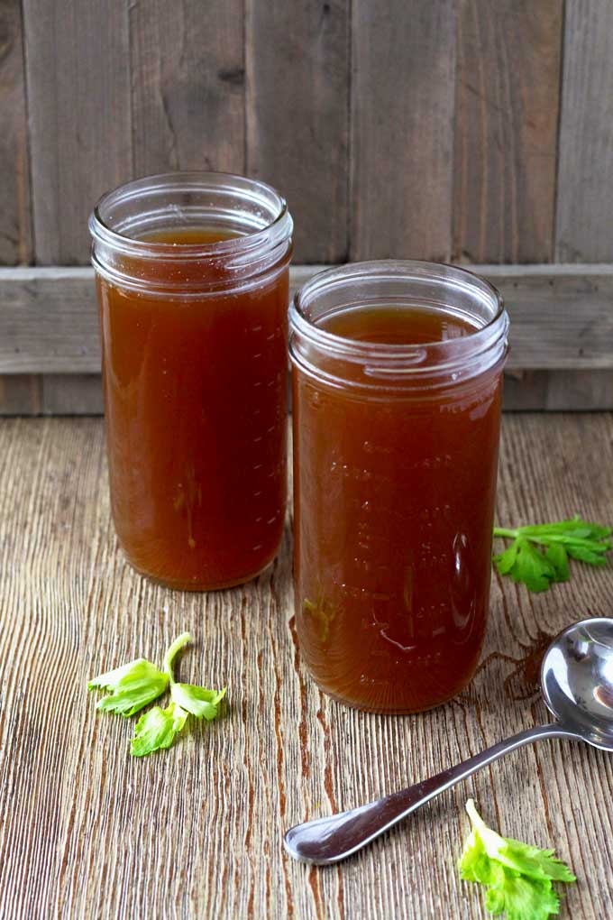 Two jars filled with beef bone broth on a wooden surface.