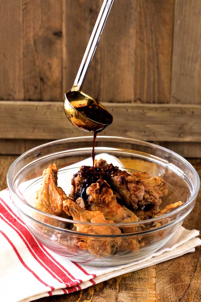 Crispy chicken wings in a clear bowl been drizzled with sauce.