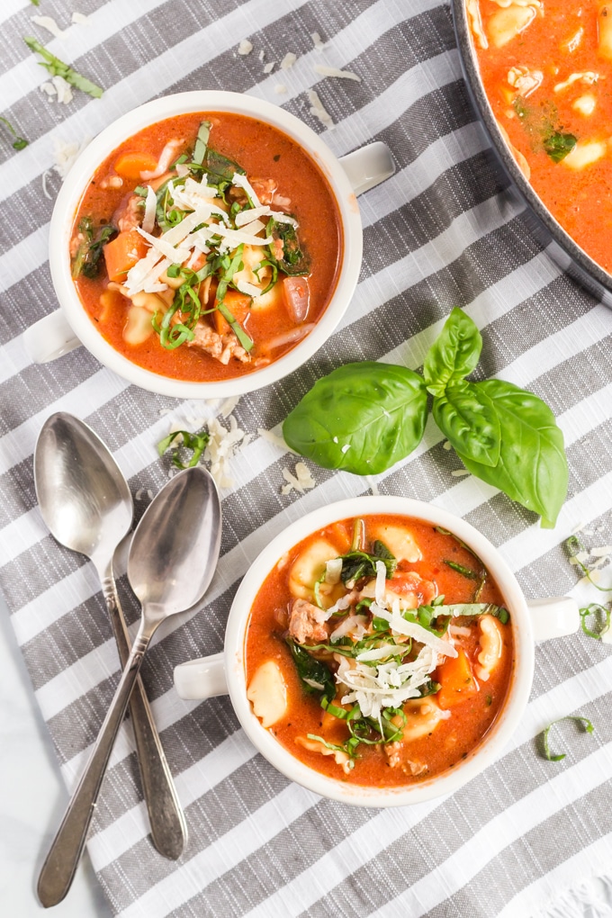 Two bowls of soup garnished with Parmesan cheese and fresh basil.