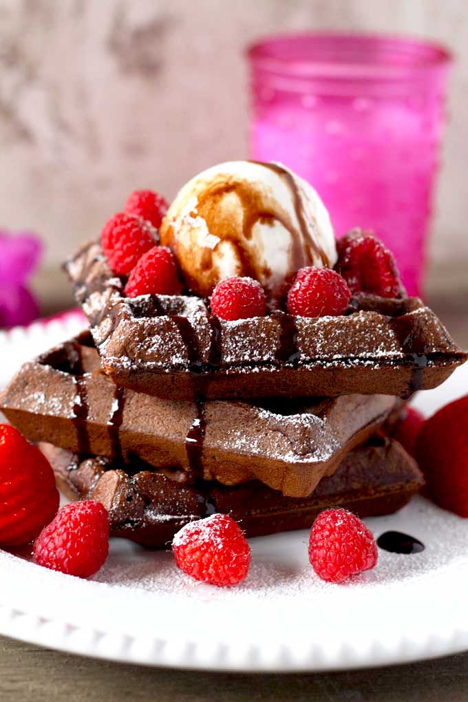 Stacked of double chocolate waffles topped with ice cream, berries and drizzled with chocolate sauce.