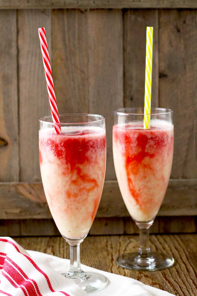 Two tall glasses with lava flow tropical cocktail on a wooden surface.