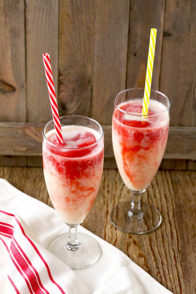 Two tall glasses filled with Lava Flow Drink on a wooden surface.