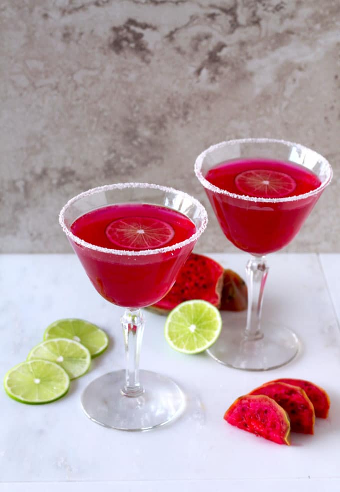 Overhead shot of two bright pink Margarita glasses with sugar on the rim and a slice of lime .