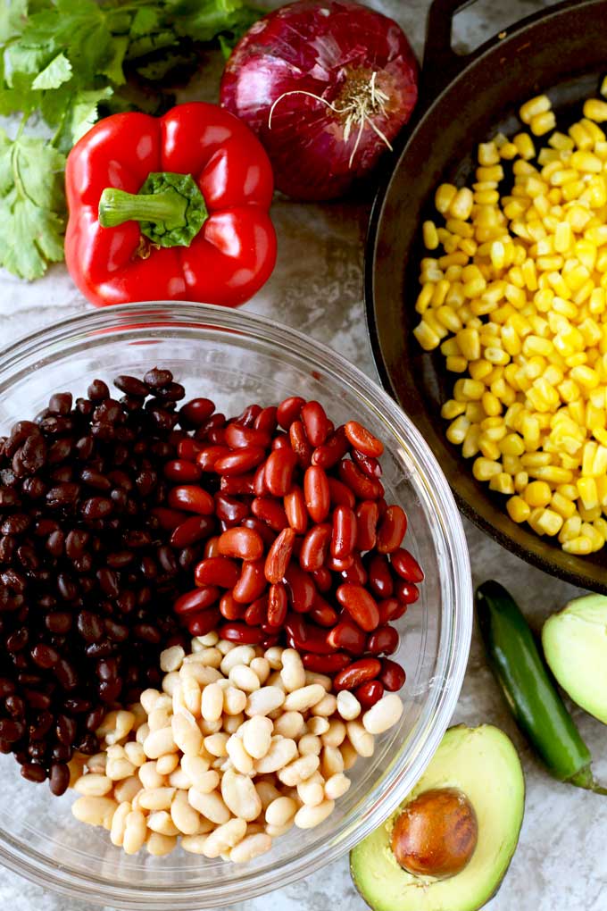 Ingredients to make bean salad on a marble surface.