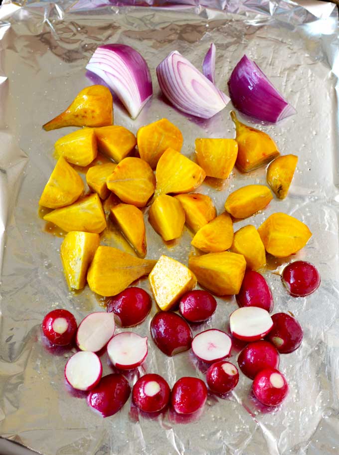 Halved radishes, golden beets and onions spread out on a sheet pan.