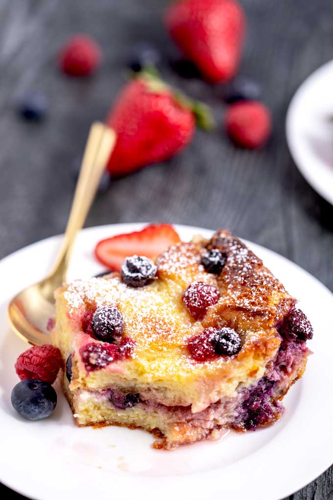 A serving of mouthwatering bread pudding loaded with berries on a white plate.