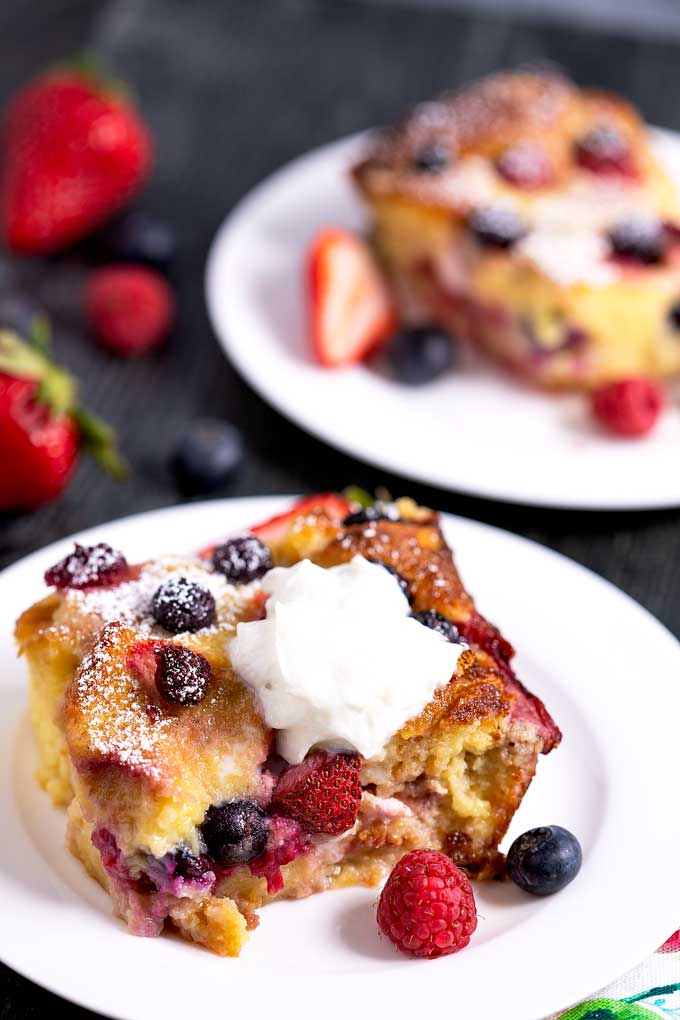 A serving of berry bread pudding topped with whipped cream on a white plate.