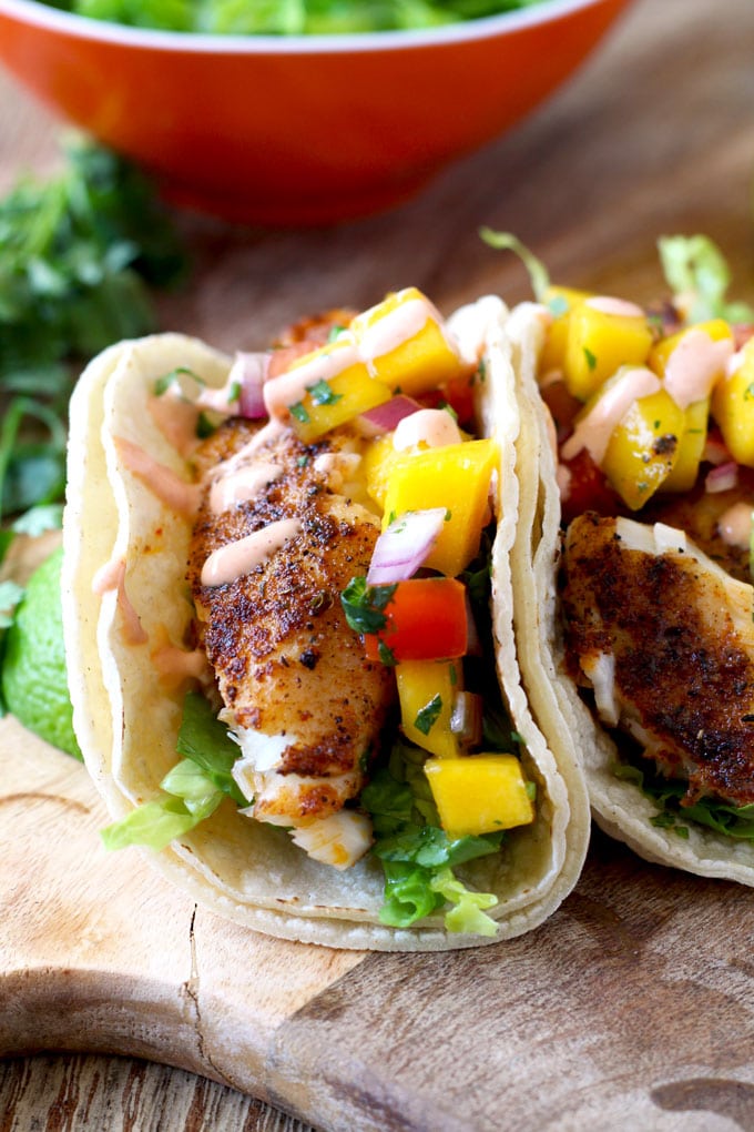 Close up of Blackened Fish Tacos with Mango Salsa and Sriracha Aioli on a wooden surface