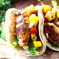 Close up of Blackened Fish Tacos with Mango Salsa and Sriracha Aioli on a wooden surface
