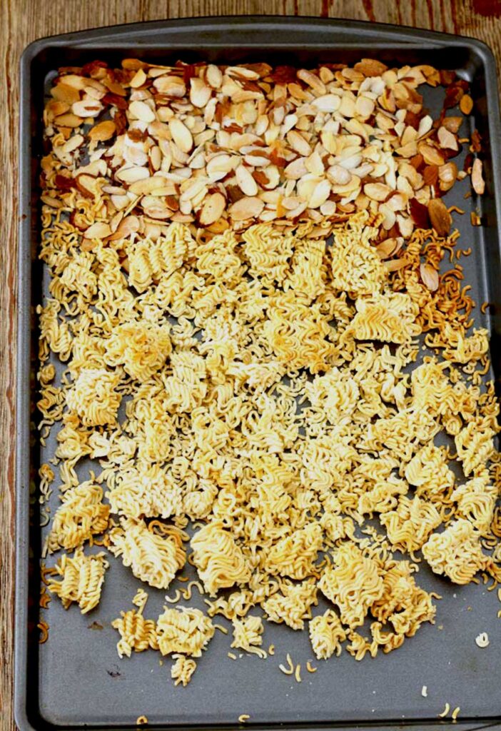 Toasted sliced almonds and dry ramen noodles on a baking sheet
