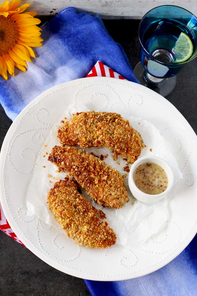 Overhead shot of three Macadamia Nut Crusted Chicken Tenders and a mini white bowl with honey mustard