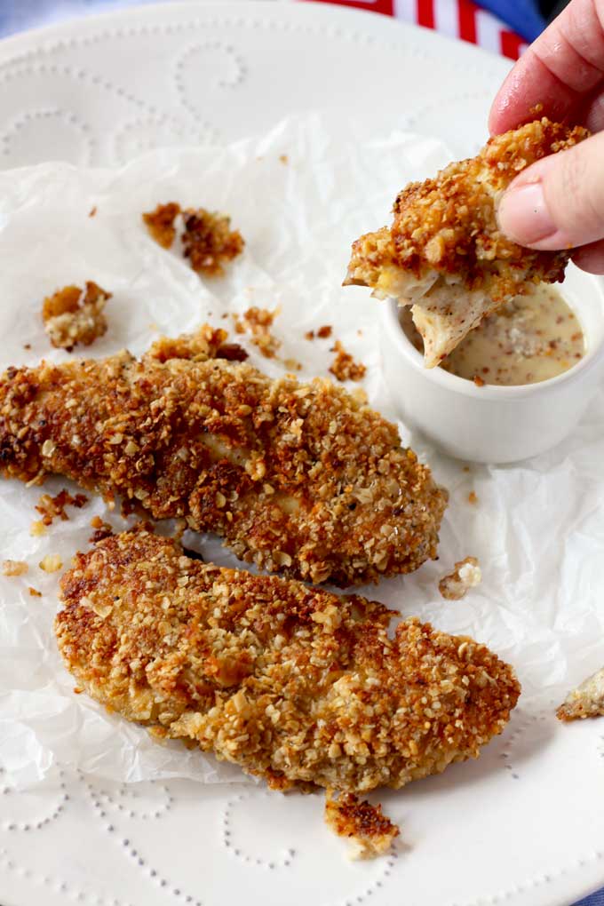 Close-up shot of three Macadamia Nut Crusted Chicken Tenders. One is been dipped in honey mustard