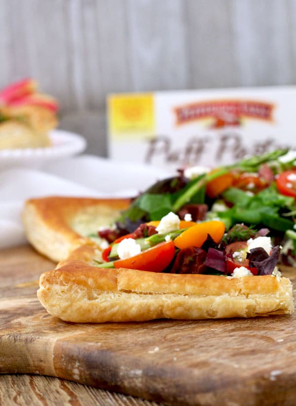 A piece of pastry tart topped with fresh salad on a wooden surface.