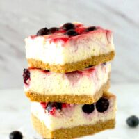 Three Berry Swirl Cheesecake Bars stacked up on a table.