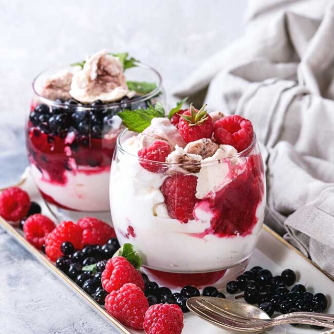 Two glasses filled with Eton mess dessert and topped with fresh raspberries and blueberries