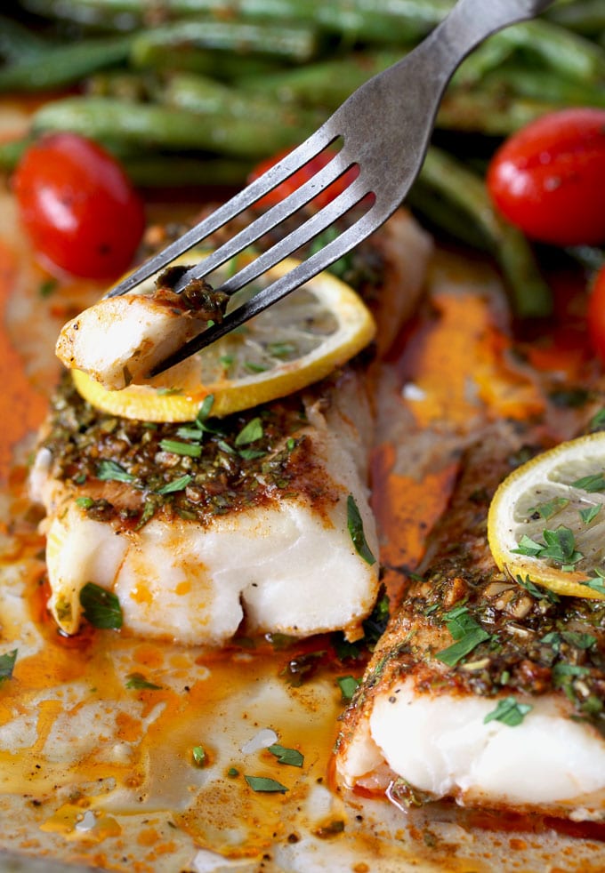 A fork picking up a piece of tender baked cod with chermoula sauce