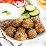 Juicy baked meatballs on a platter with Tzatziki sauce and cucumbers