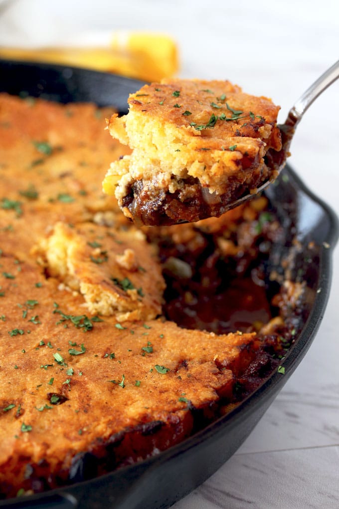 View of a serving spoon scooping a portion of tamale pie off a cast iron skillet