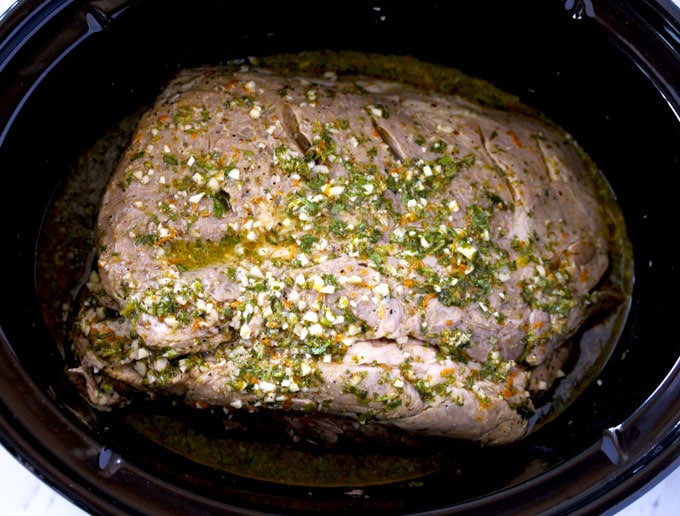 Top view of a pork roast (pork shoulder) inside a slow cooker, marinated and covered with Mojo sauce.