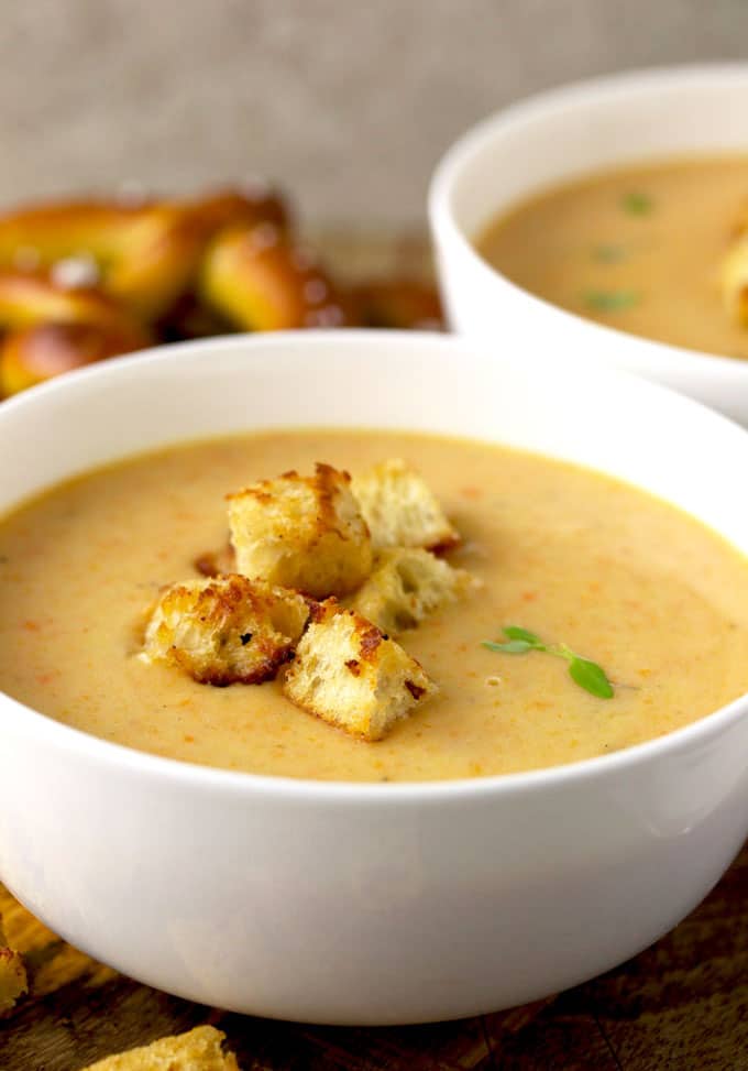 A close-up view of creamy Cheddar Ale Soup topped with crispy croutons served on a white soup bowl. Garnished with 2 thyme leaves