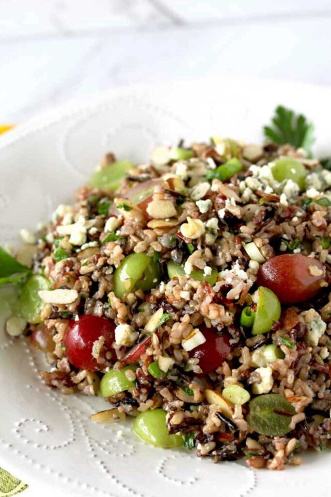 Cold wild rice salad with grapes and almonds on a white plate