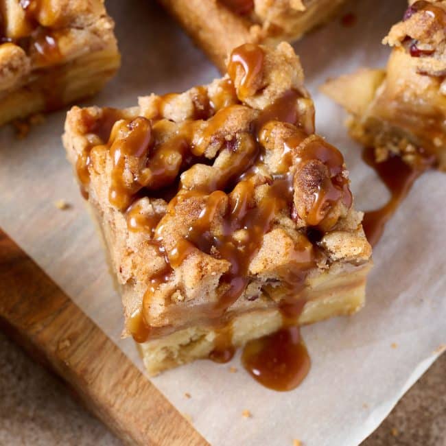Close up side view of an apple pie bar with a pecan crumble and drizzled with salted caramel