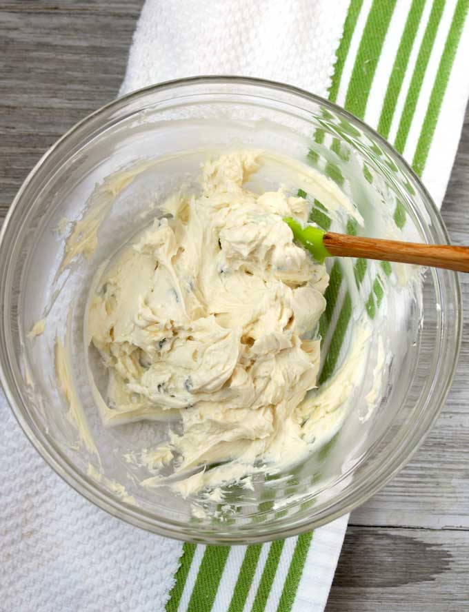 View of a bowl filled with a mixture of cream cheese goat cheese, honey and thyme on a white wooden board.