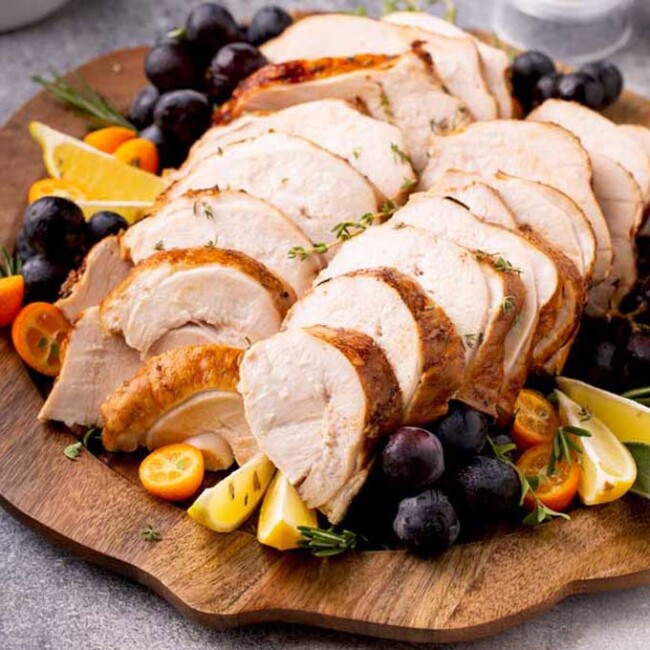 Sliced turkey breast in a wooden tray garnished with herbs and fruits
