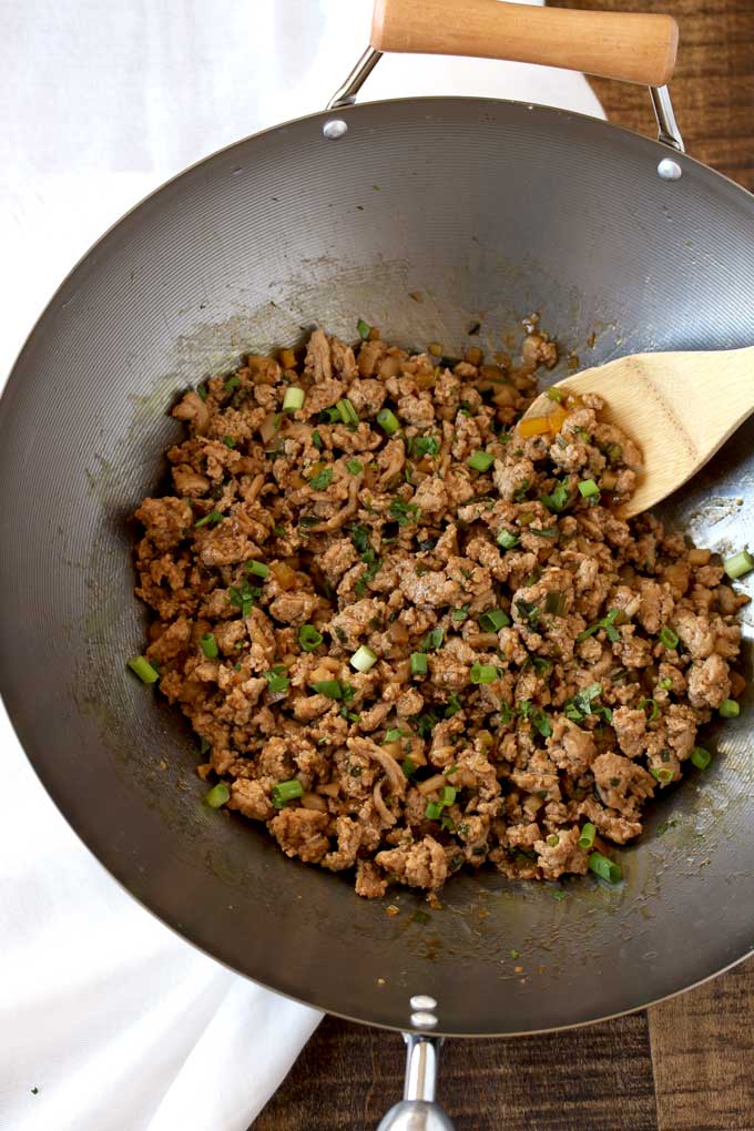 View of a wok filled with ground chicken, chopped garlic, ginger, yellow bell pepper and garnished with chopped cilantro.