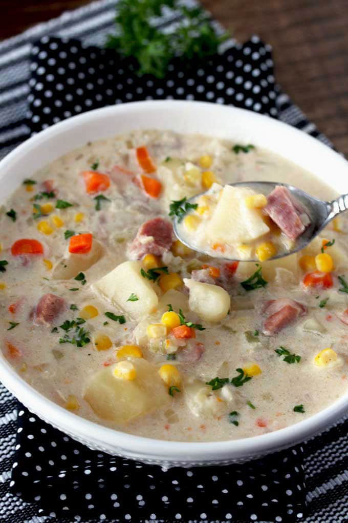 Pictured here a spoon scooping hearty and creamy potato and ham soup from a soup bowl.