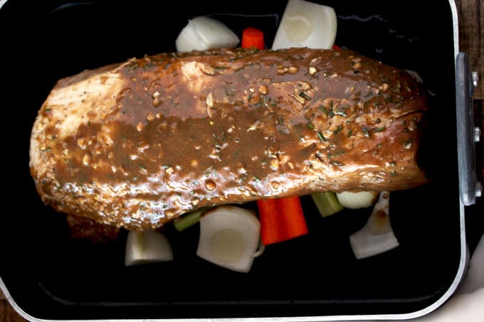 A raw pork loin roast sitting on top of carrots, onions and celery inside a roasting pan