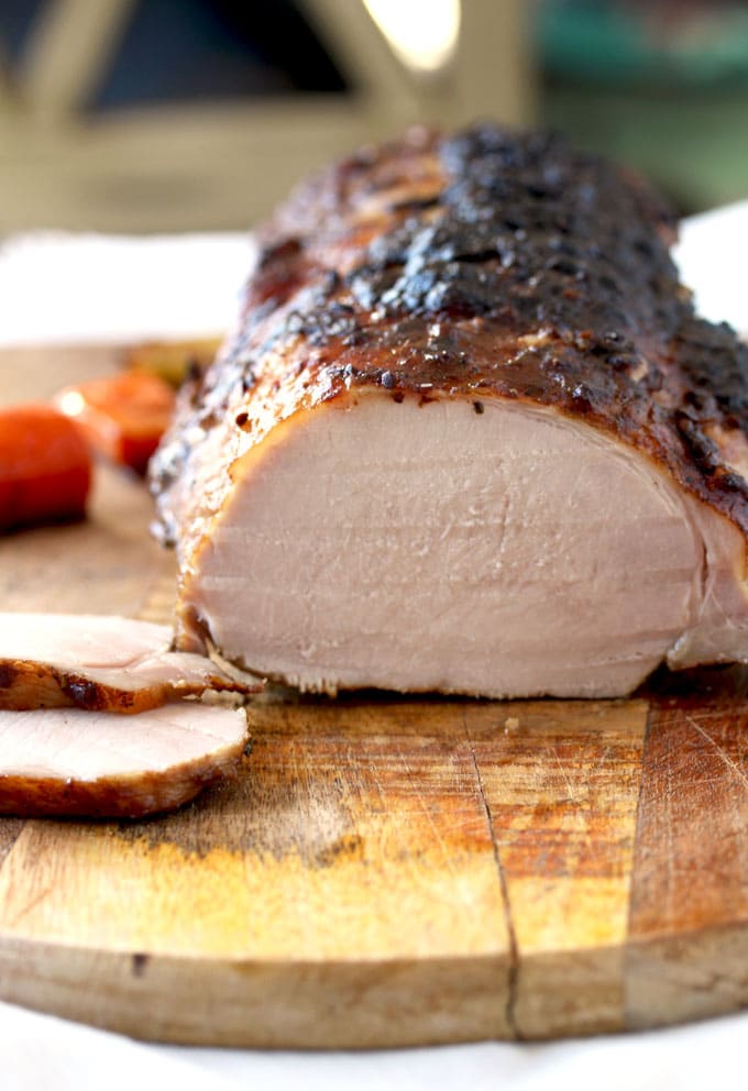 Close up view of the Oven Roasted Pork Loin on a cutting board. The roast has been sliced and you can see 2 slices laying on the side of the roast