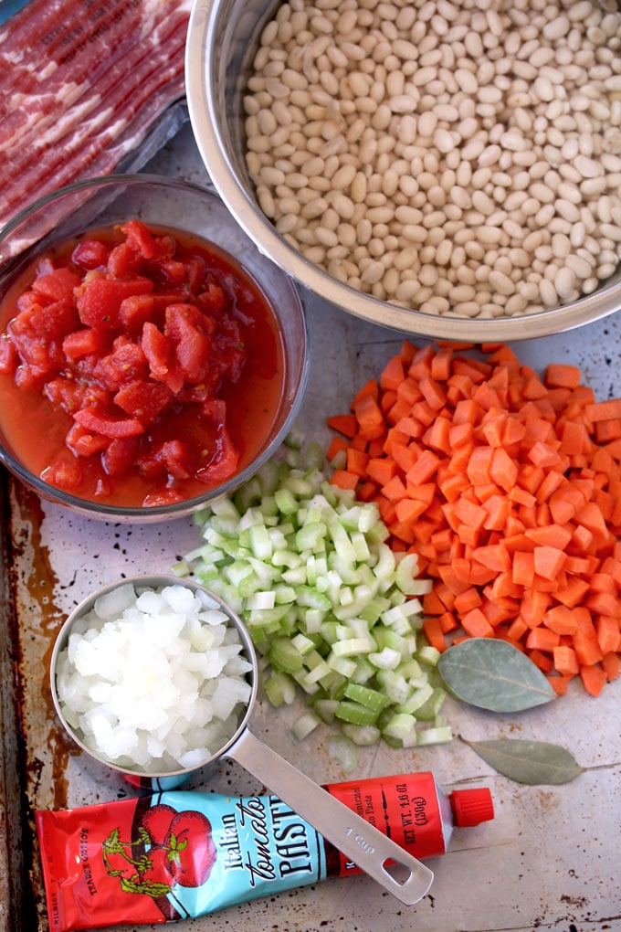 Pictured here are the ingredients for making Bean and Bacon soup. White beans, chopped carrots, celery and onions. Diced tomatoes, tomato paste, bacon and bay leaves.