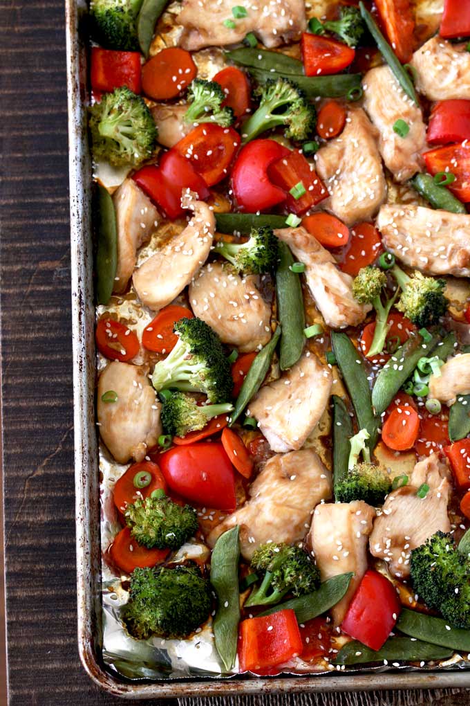 Pictured here a sheet pan with Asian Chicken Stir Fry and vegetables, broccoli florets, red bell peppers, sliced carrots and sugar snap peas.