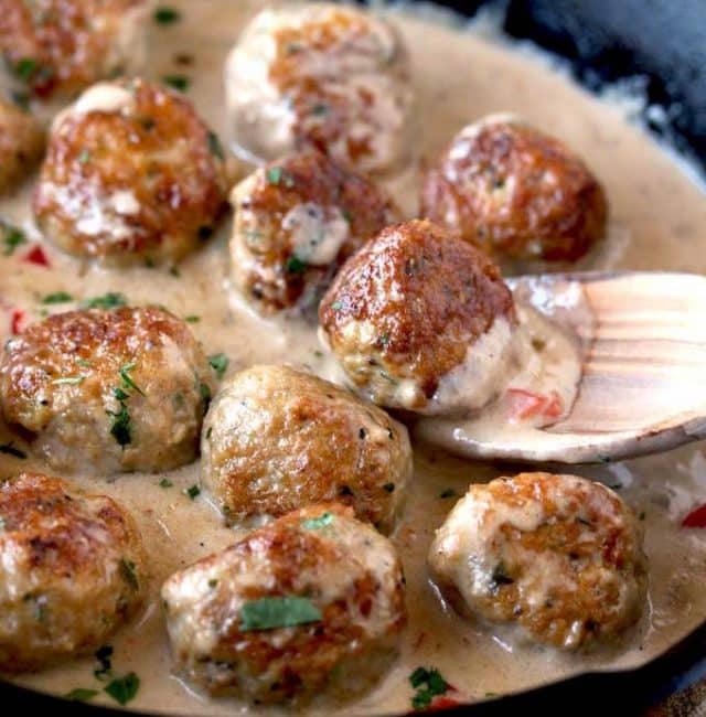 Close up view of a chicken meatball scooped up with a wooden spoon from a cast iron skillet