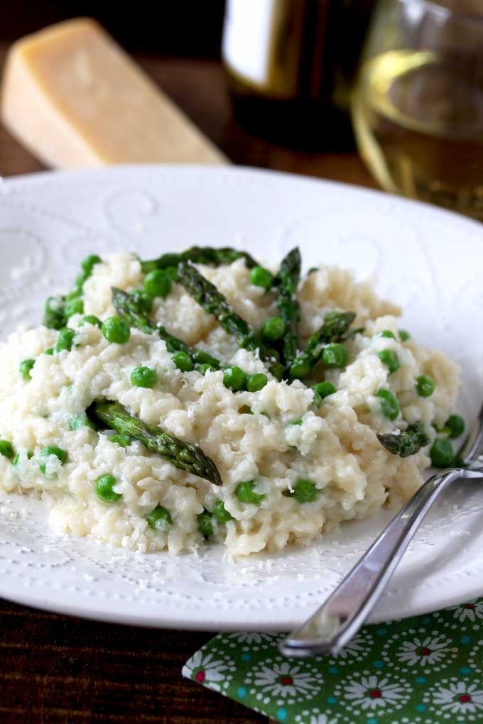 View of Parmesan, Peas and Asparagus Risotto garnished with shredded Parmesan cheese on a white plate.