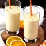 Pictured here two tall glasses filled with Orange Honey Lassi with two orange polka dot straws