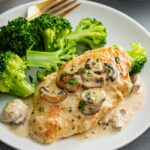 Chicken breast cutlet in mushroom cream sauce served with broccoli on a white plate