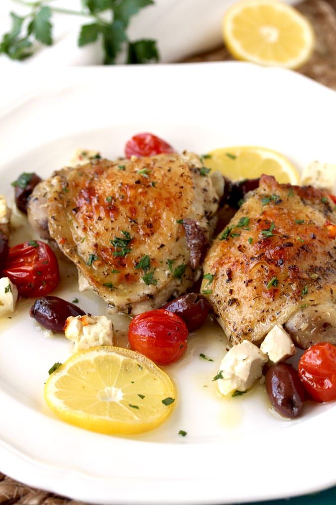 Greek Lemon Oven Roasted Chicken Thighs pieces served on a white plate. Garnished with lemon slices